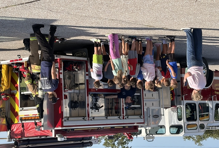 Students listen to firefighters near firetruck.