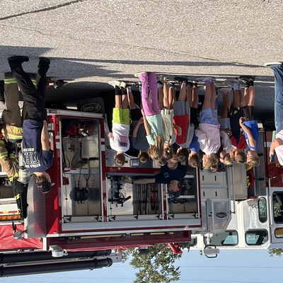 Students listen to firefighters near firetruck.