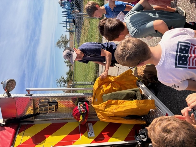 Students listen to firefighters near firetruck.