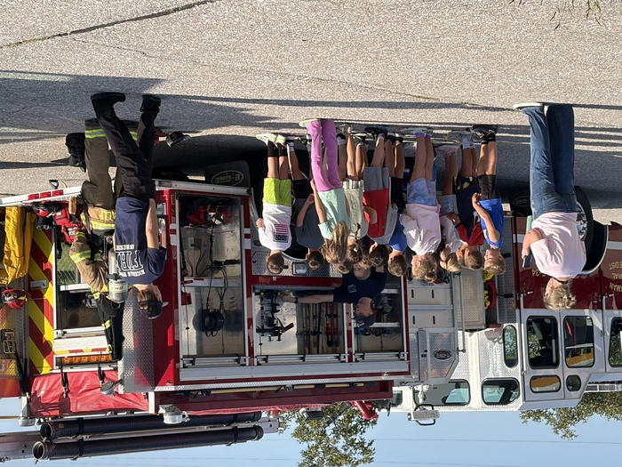Students listen to firefighters near firetruck.