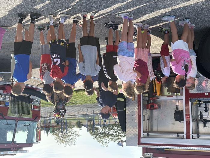 Students listen to firefighters near firetruck.