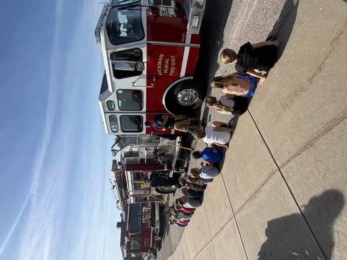 Students listen to firefighters near firetruck.